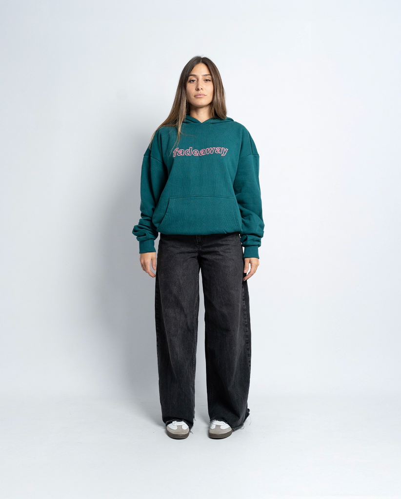 Modelo femenina vistiendo la sudadera verde oversize con bordado 3D rosa, vista frontal.